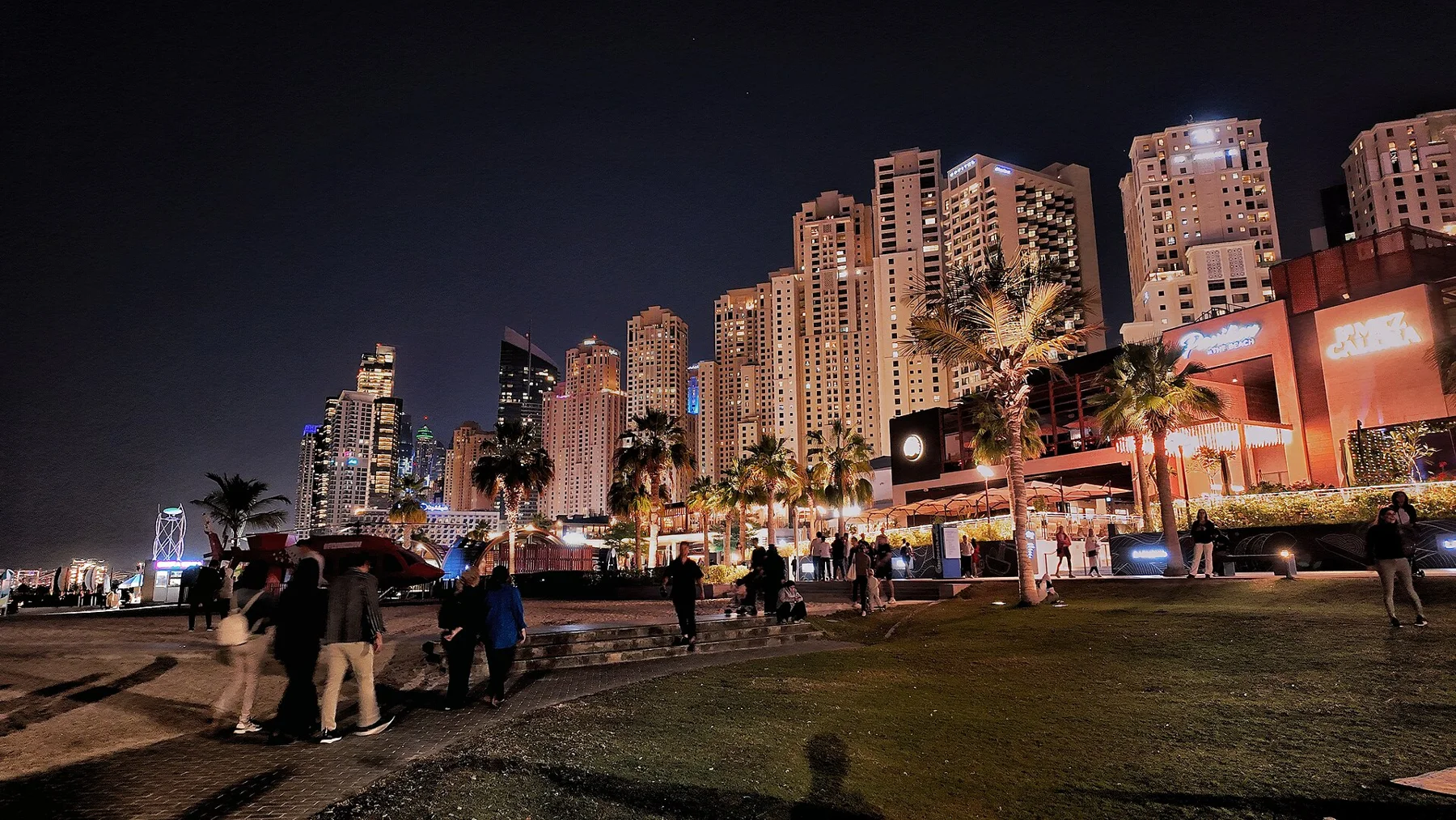 People walking beside the illuminated JBR beachfront towers at night