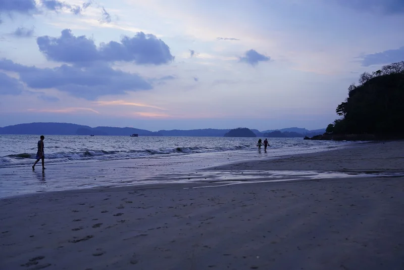 People walking along Ao Nang Beach as the sun sets over the Andaman Sea